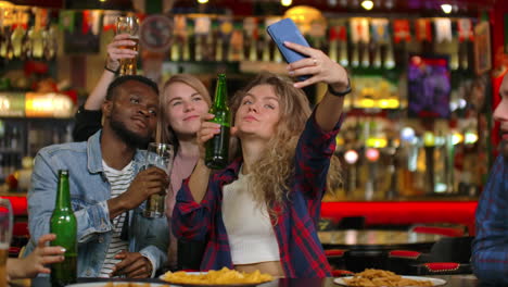 Los-Amigos-Se-Toman-Selfies-Con-Un-Smartphone-En-El-Bar.-Los-Jóvenes-Posan-Riendo-Y-Hablando.-Botellas-De-Cerveza-Y.-Amigos-Se-Toman-Selfies-Con-Un-Teléfono-Inteligente-En